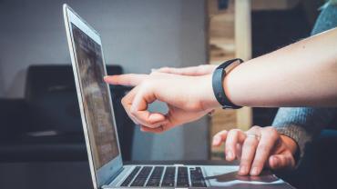 Imatge de dues persones senyalant la pantalla d'un portatil