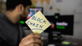 Imatge d'un informàtic ensenyant un post-it amb 'Blockchain'.